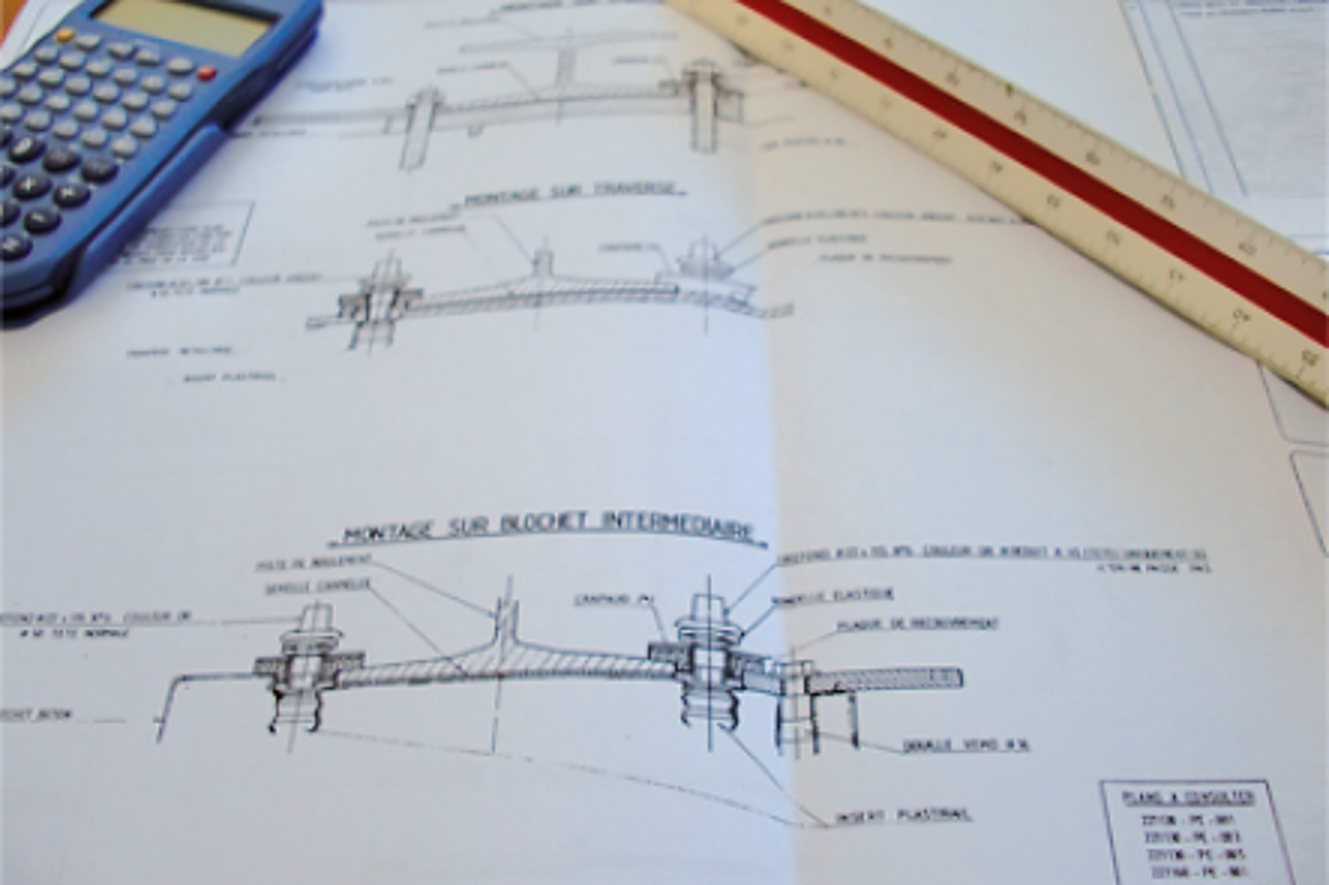 Plans techniques en français posés sur une table, avec une calculatrice bleue et une règle d'échelle rouge et blanche.